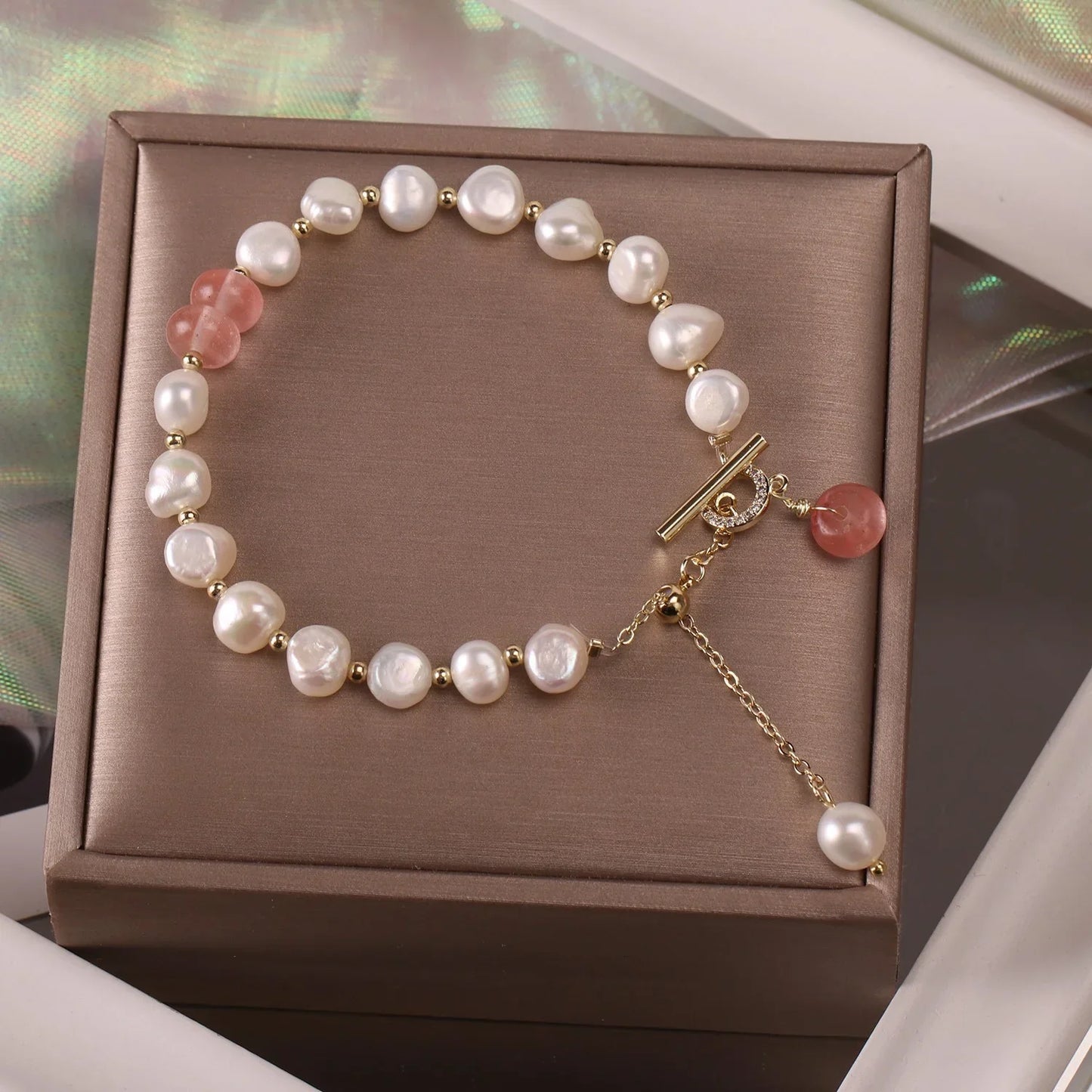 Elegant freshwater pearl bracelet with gold beads and pink gemstone on brown jewelry box