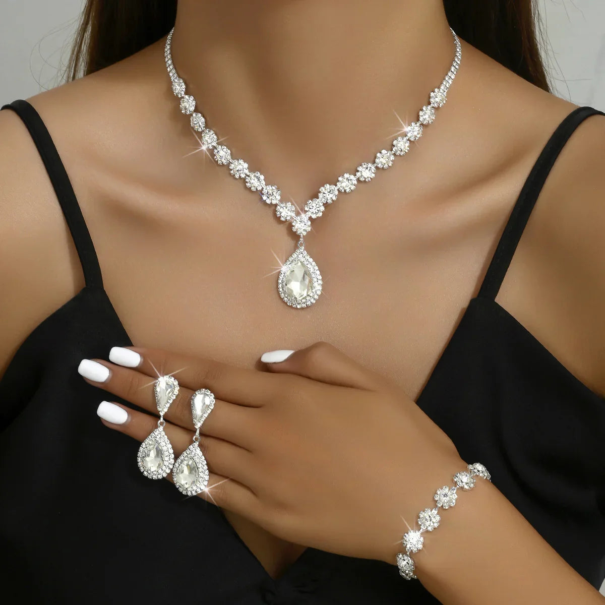 Elegant clear crystal jewelry set with necklace, teardrop earrings, and bracelet on woman in black dress