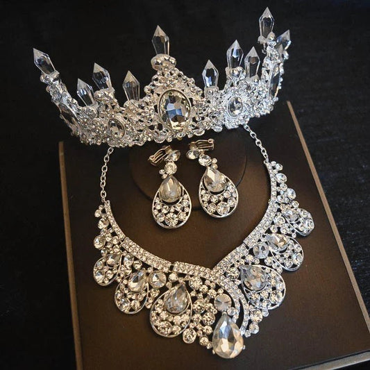 silver crystal crown, necklace, and matching earrings set on black background