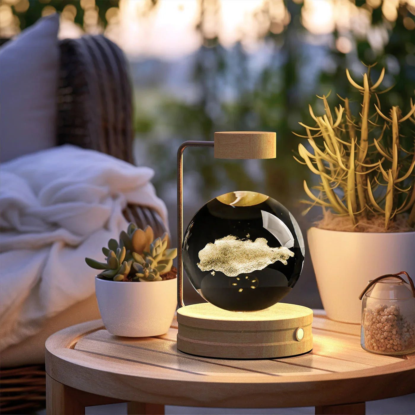 Levitating glass orb with gold dust on wooden base lamp on round wooden table with succulents