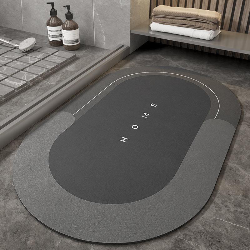 Modern bathroom with gray oval bath mat labeled HOME on marble floor near glass shower and shelves with folded towels