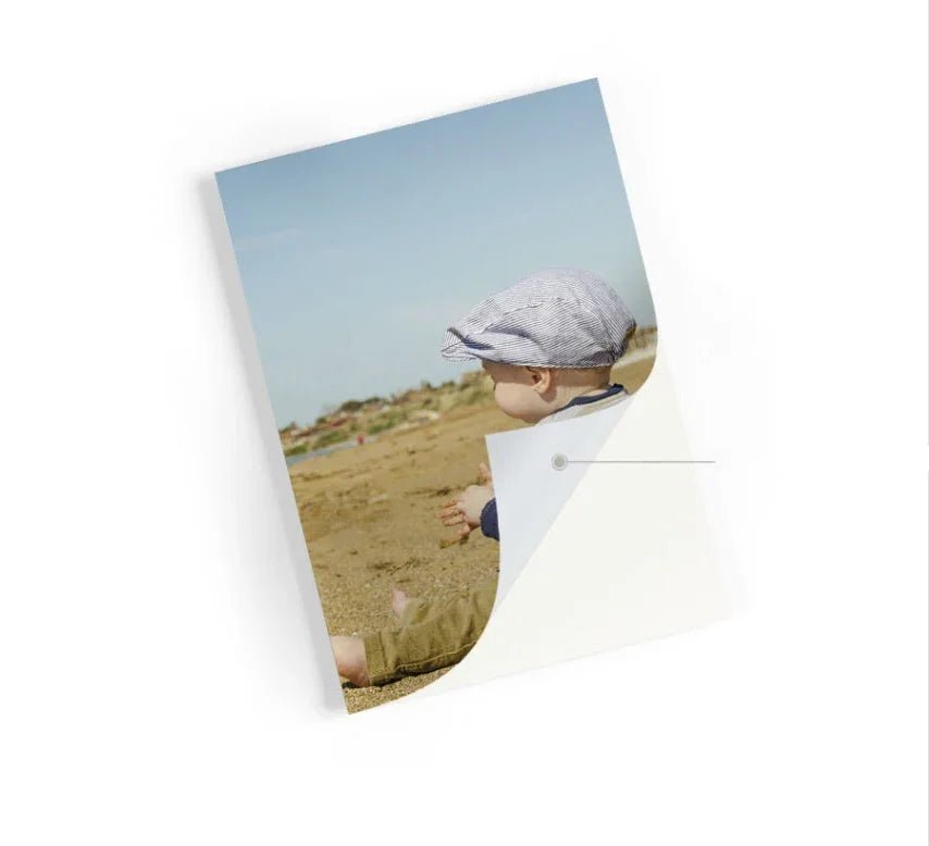 Photo of a baby wearing a striped cap sitting on a sandy beach under clear blue sky