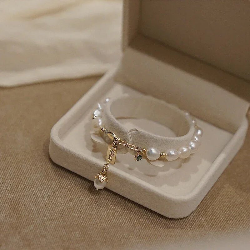 Elegant pearl bracelet with gold chain and charm in beige jewelry box on fabric surface