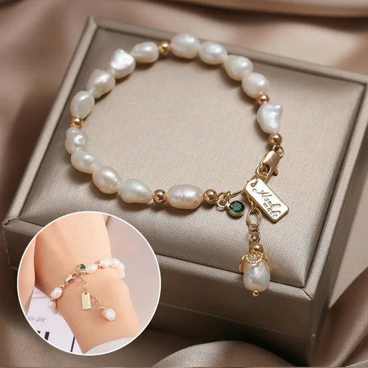 Elegant white pearl bracelet with gold beads, green gem charm, and gold name tag on beige box