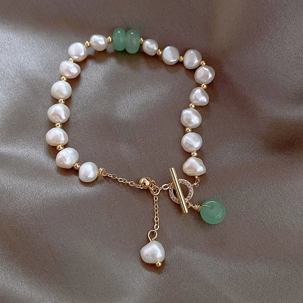 Irregular white pearl bracelet with gold beads and green gemstone detail on gray satin fabric