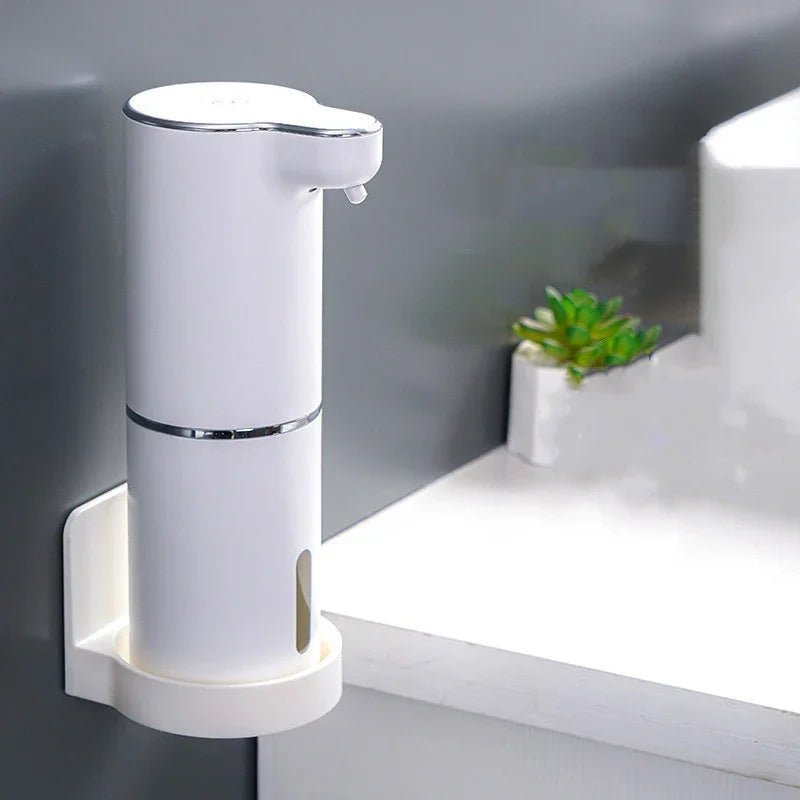 White automatic soap dispenser mounted on dark wall near white countertop with small green plant