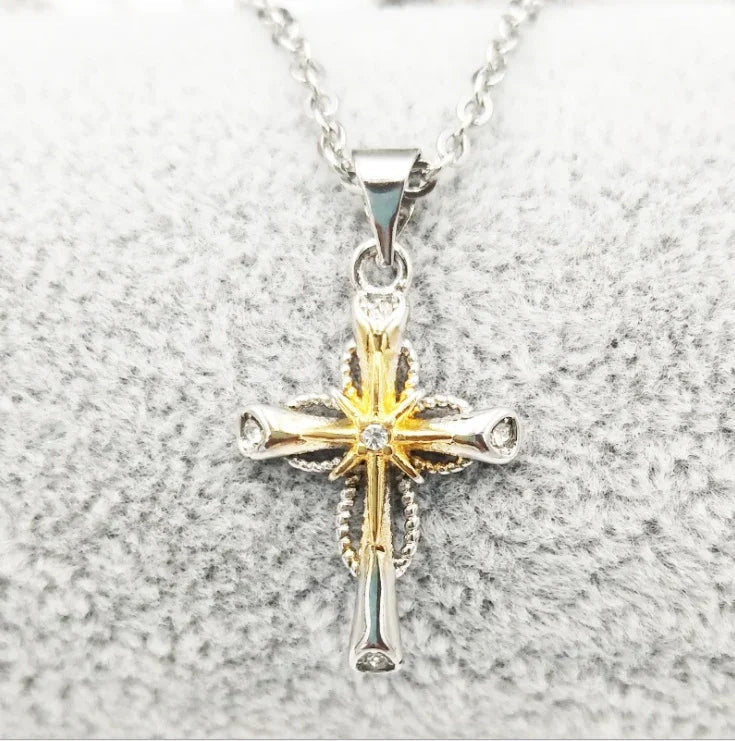 Silver and gold cross pendant necklace with intricate design and gemstone center on soft gray fabric