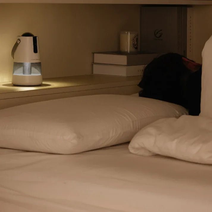 Modern white bedside humidifier emitting light next to person sleeping in cozy bed with beige pillow