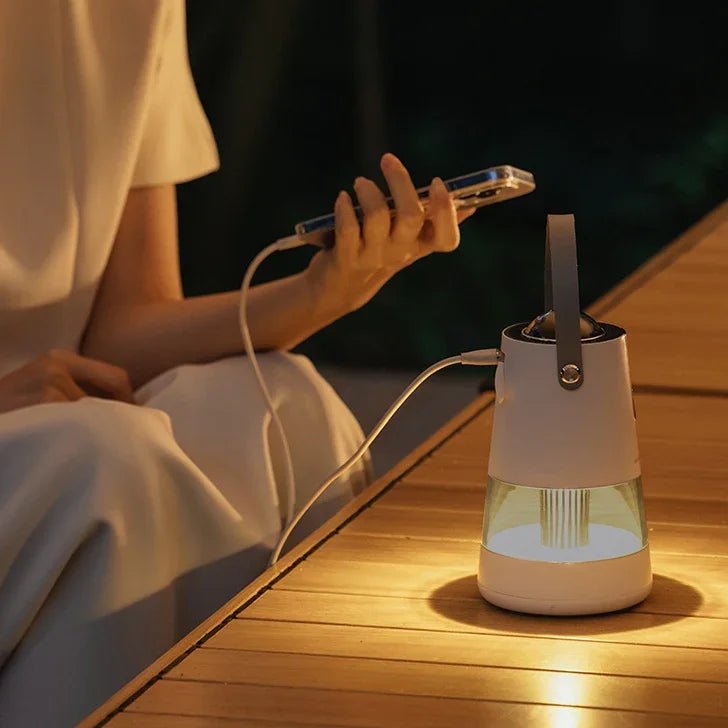 Person holding smartphone charging a modern portable LED lantern on wooden table at night